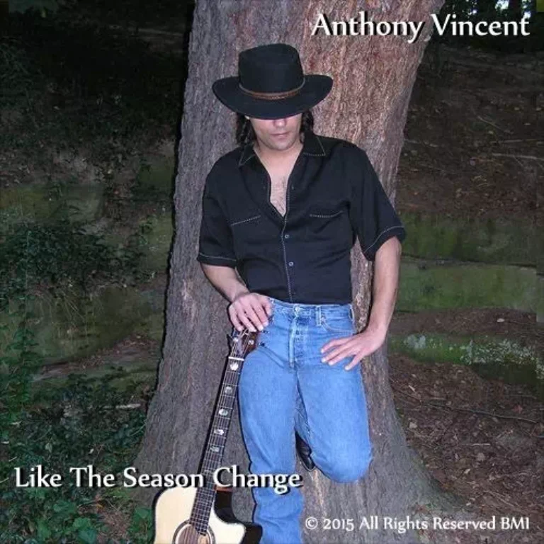 Anthony leaning on a tree in cowboy hat, acoustic guitar beside him.